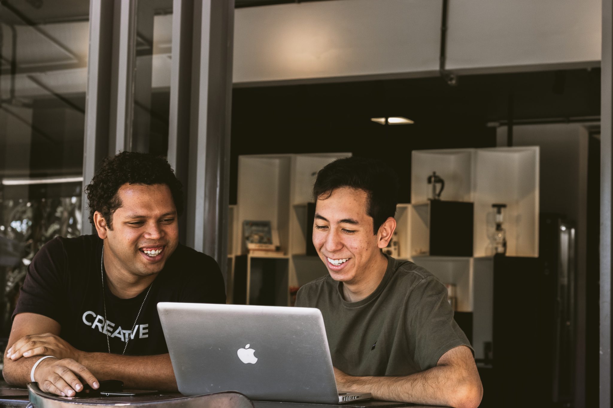two men in their 20s or 30s smiling and working on a laptop in a modern office or co-working space